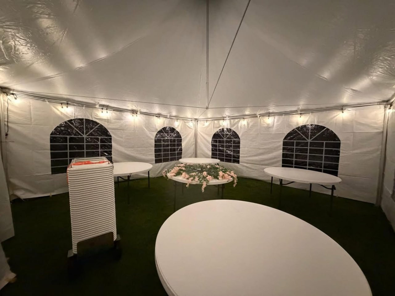 Tables set up inside a white event tent with sidewalls and string lighting