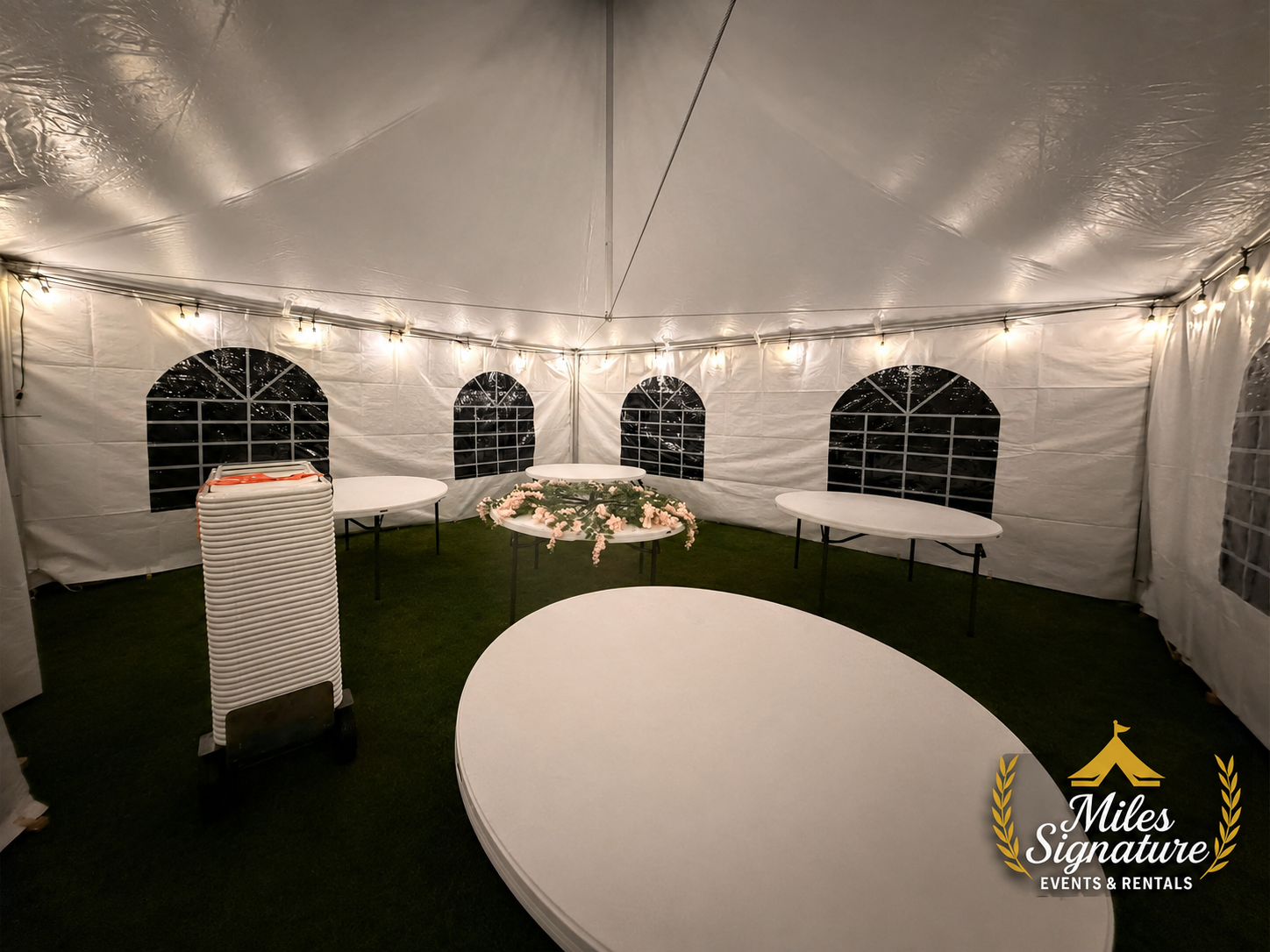 Tables and chairs arranged inside a lit event tent
